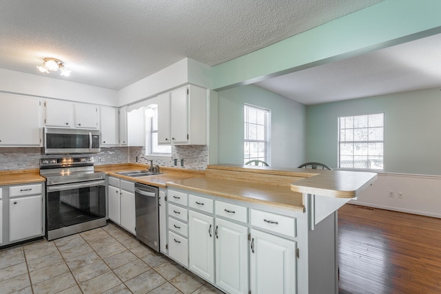 kitchen with white cabinets, light hardwood / wood-style floors, kitchen peninsula, and appliances with stainless steel finishes