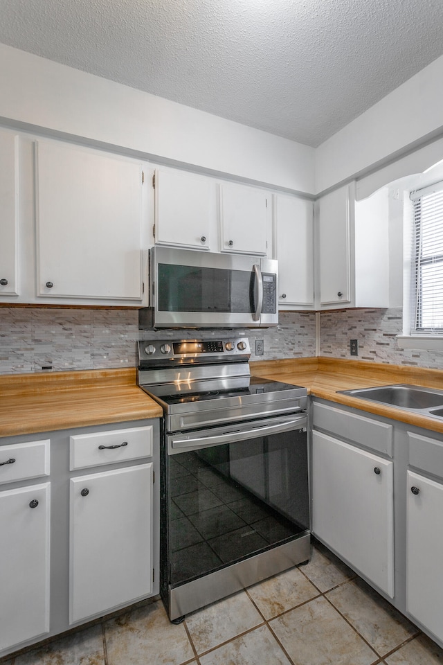 kitchen with white cabinets, light tile patterned floors, appliances with stainless steel finishes, and tasteful backsplash