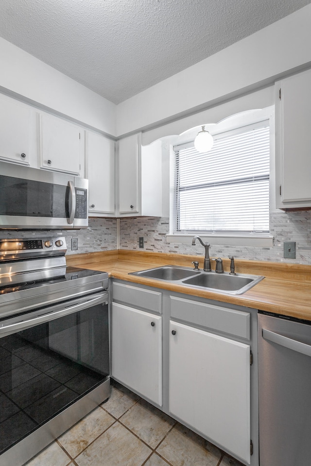 kitchen with sink, light tile patterned flooring, backsplash, white cabinets, and appliances with stainless steel finishes