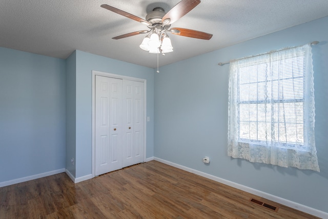 unfurnished bedroom featuring a textured ceiling, a closet, ceiling fan, and dark wood-type flooring