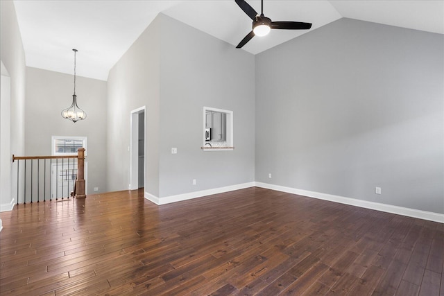 unfurnished living room with ceiling fan with notable chandelier, high vaulted ceiling, and dark hardwood / wood-style floors