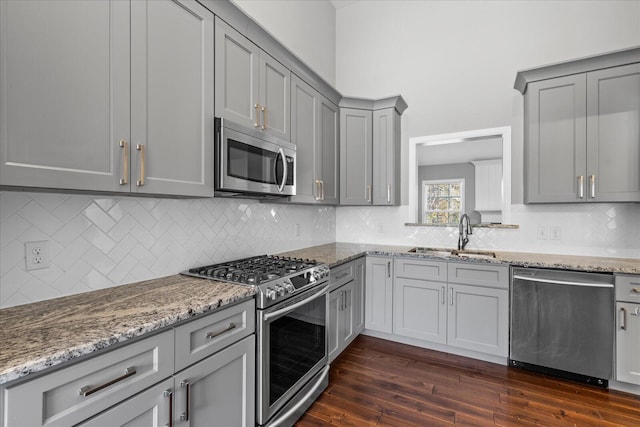 kitchen featuring light stone countertops, sink, tasteful backsplash, dark hardwood / wood-style flooring, and appliances with stainless steel finishes