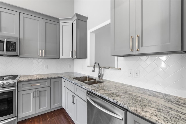 kitchen with appliances with stainless steel finishes, dark hardwood / wood-style flooring, light stone counters, sink, and gray cabinets