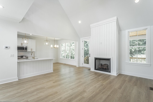 unfurnished living room featuring a fireplace, high vaulted ceiling, light hardwood / wood-style floors, and sink