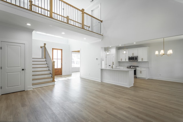 unfurnished living room with light wood-type flooring, sink, a high ceiling, and a chandelier