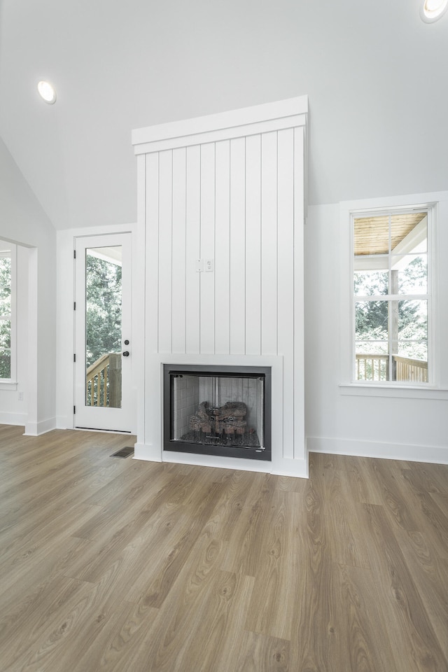 unfurnished living room with a healthy amount of sunlight, light wood-type flooring, and vaulted ceiling