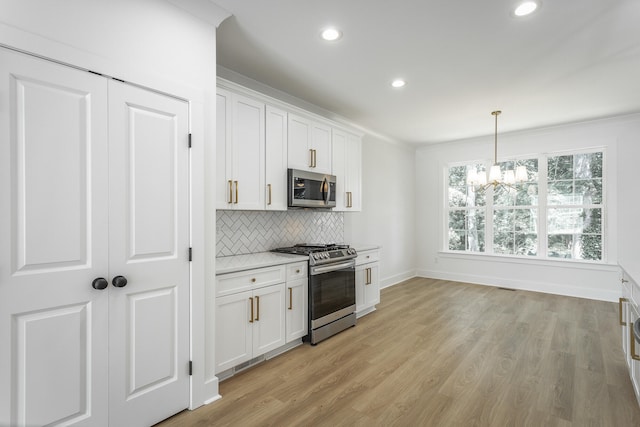 kitchen with backsplash, hanging light fixtures, appliances with stainless steel finishes, light hardwood / wood-style floors, and white cabinetry