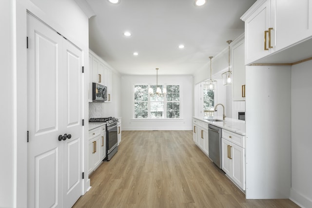 kitchen with white cabinetry, light stone countertops, sink, stainless steel appliances, and decorative light fixtures