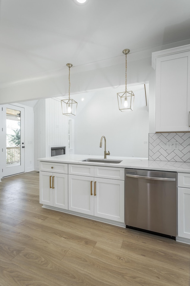 kitchen featuring stainless steel dishwasher, white cabinets, sink, and hanging light fixtures