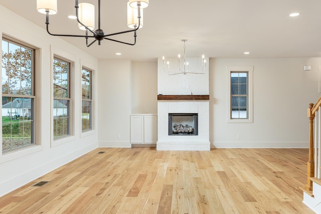 unfurnished living room with a fireplace, light hardwood / wood-style floors, an inviting chandelier, and plenty of natural light