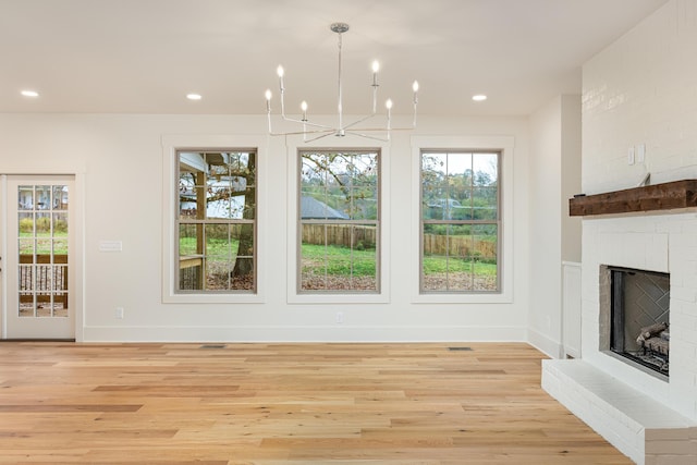 unfurnished dining area featuring a fireplace, a chandelier, and light hardwood / wood-style flooring