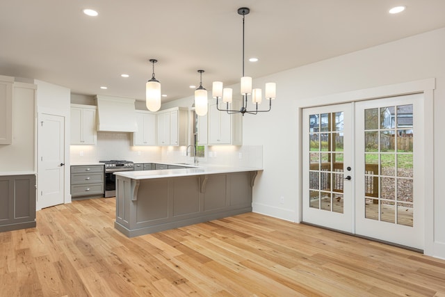 kitchen with white cabinetry, stainless steel range with gas cooktop, kitchen peninsula, custom exhaust hood, and light wood-type flooring