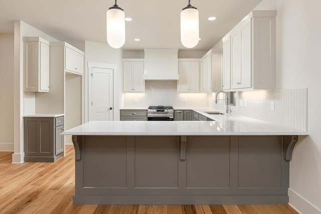 kitchen featuring pendant lighting, custom range hood, sink, and light hardwood / wood-style flooring