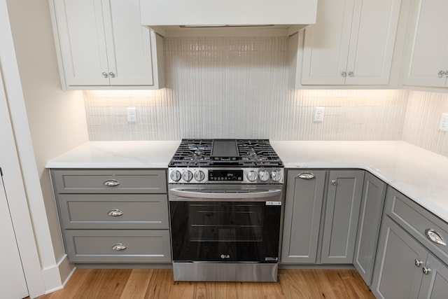 kitchen featuring stainless steel gas stove, backsplash, extractor fan, gray cabinets, and light wood-type flooring