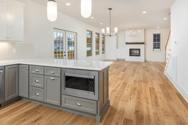 kitchen with stainless steel microwave, light hardwood / wood-style flooring, gray cabinets, a fireplace, and kitchen peninsula