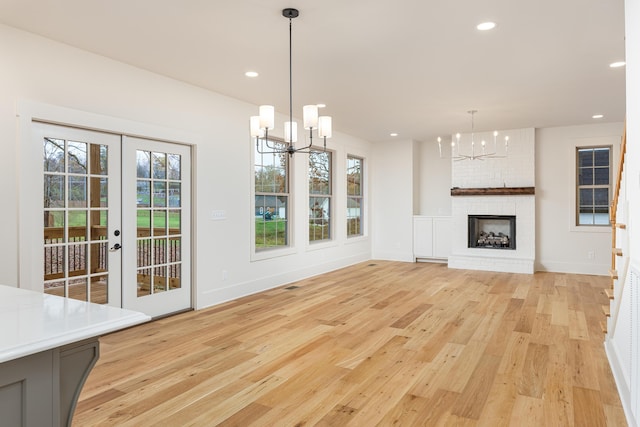 unfurnished living room featuring a fireplace, french doors, light hardwood / wood-style floors, and an inviting chandelier