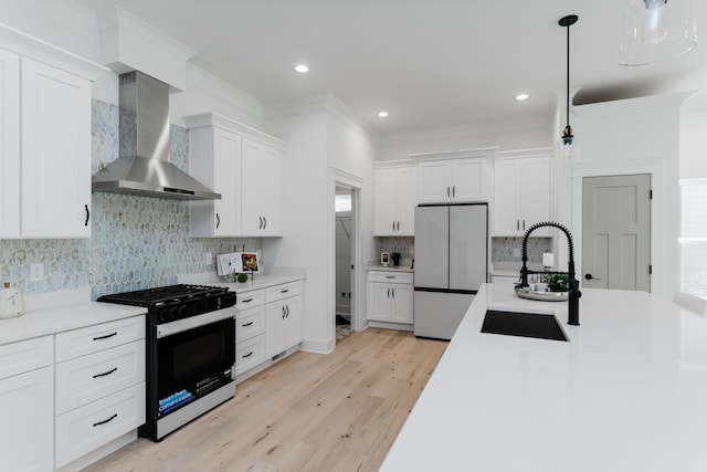 kitchen featuring pendant lighting, wall chimney range hood, sink, white cabinetry, and stainless steel range with gas stovetop