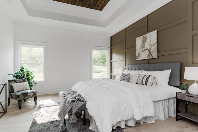 bedroom with a tray ceiling, light hardwood / wood-style flooring, and multiple windows