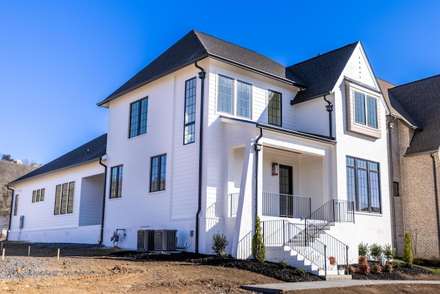 view of side of property featuring covered porch, brick siding, central AC unit, and stairs