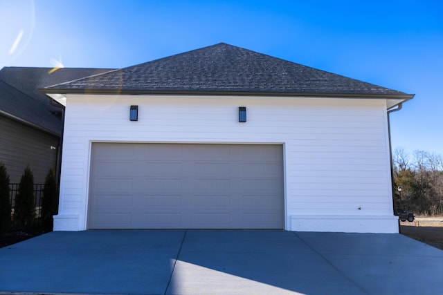 exterior space with a garage, driveway, roof with shingles, and an outbuilding