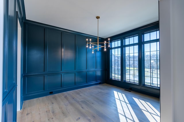 spare room with light wood finished floors, visible vents, a decorative wall, and a notable chandelier