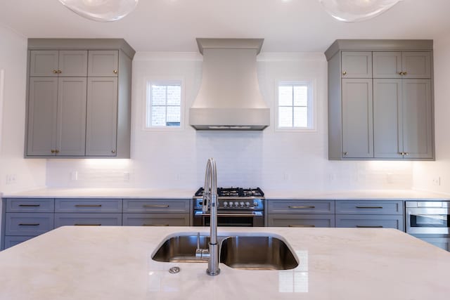 kitchen featuring high end stove, gray cabinetry, a healthy amount of sunlight, and custom exhaust hood