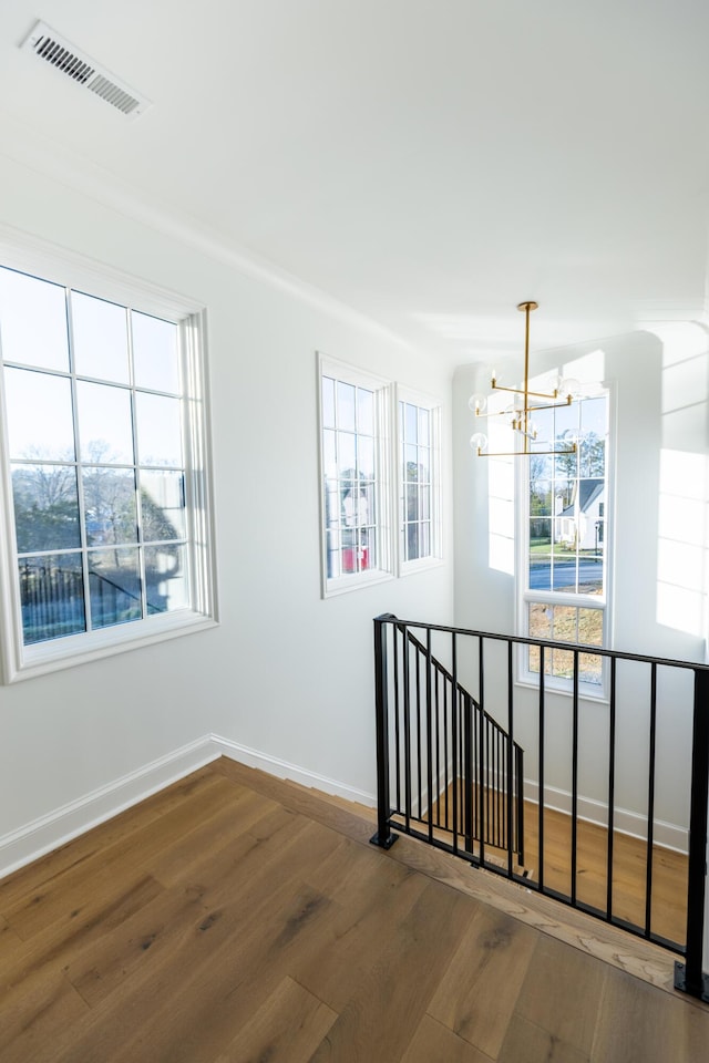 empty room with wood-type flooring, visible vents, a chandelier, and baseboards