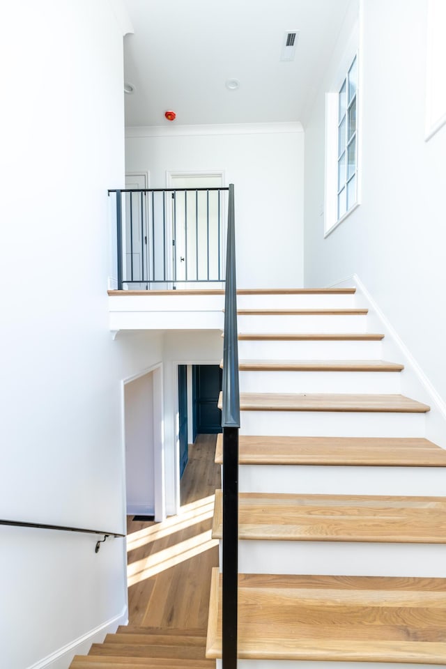 staircase with ornamental molding, visible vents, and wood finished floors