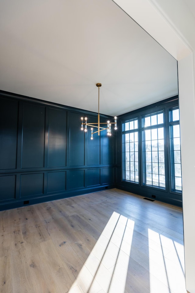 unfurnished dining area featuring a notable chandelier, wood finished floors, visible vents, and a decorative wall