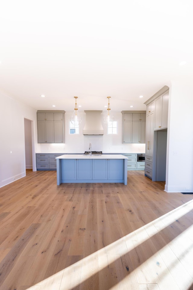 kitchen featuring light wood-style floors, gray cabinets, an island with sink, and custom exhaust hood