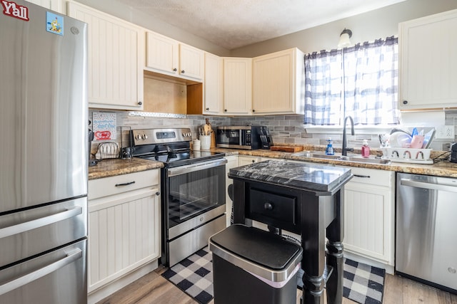 kitchen with light stone countertops, a textured ceiling, stainless steel appliances, sink, and light hardwood / wood-style flooring