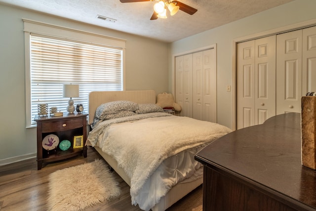 bedroom featuring ceiling fan, wood-type flooring, a textured ceiling, and multiple closets