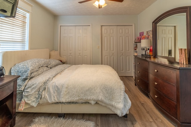 bedroom with wood-type flooring, a textured ceiling, two closets, and ceiling fan