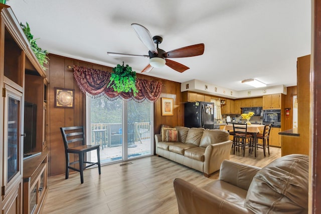 living room featuring wood walls, ceiling fan, and light wood-type flooring