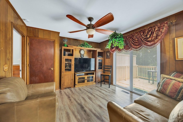 living room featuring wooden walls, ceiling fan, and light hardwood / wood-style floors