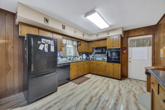 kitchen featuring backsplash, black appliances, sink, wooden walls, and light hardwood / wood-style floors