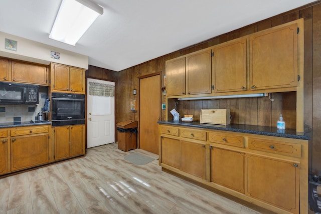 kitchen with wood walls, backsplash, black appliances, vaulted ceiling, and light hardwood / wood-style flooring