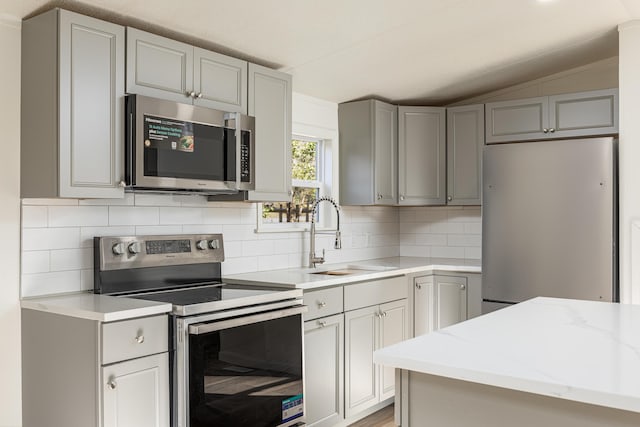 kitchen with sink, light stone counters, vaulted ceiling, gray cabinets, and appliances with stainless steel finishes