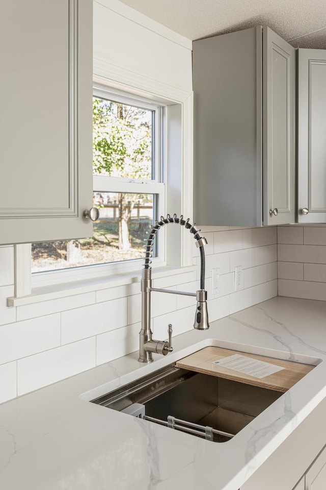 room details with gray cabinetry, decorative backsplash, light stone counters, and sink