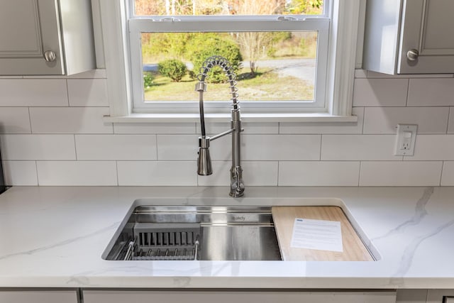 details with tasteful backsplash, gray cabinetry, light stone counters, and sink