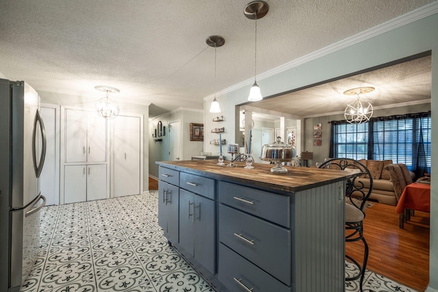 kitchen with ornamental molding, a chandelier, butcher block countertops, stainless steel refrigerator, and a breakfast bar area