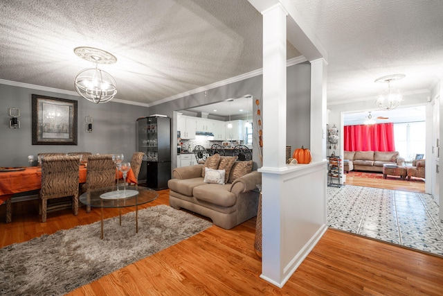 living room featuring an inviting chandelier, crown molding, a textured ceiling, and light hardwood / wood-style flooring