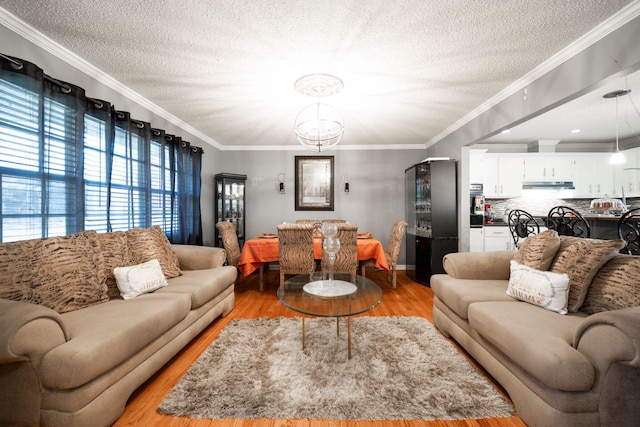 living room with a textured ceiling, light hardwood / wood-style flooring, ornamental molding, and a notable chandelier