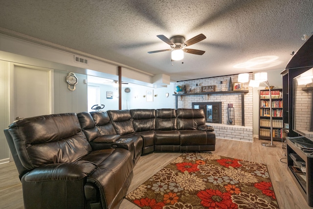 living room with a brick fireplace, a textured ceiling, brick wall, and light hardwood / wood-style flooring