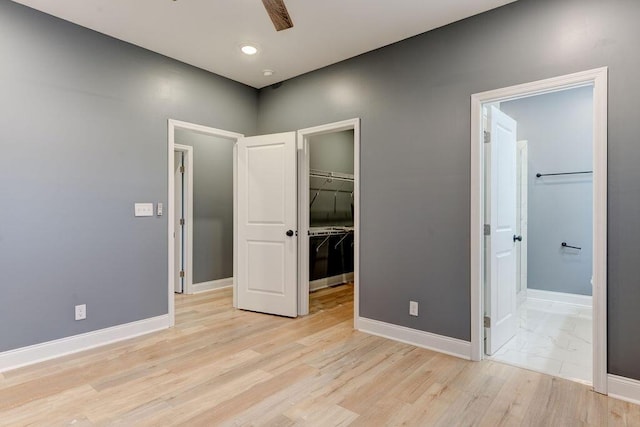 unfurnished bedroom with a closet, a walk in closet, ceiling fan, and light hardwood / wood-style flooring