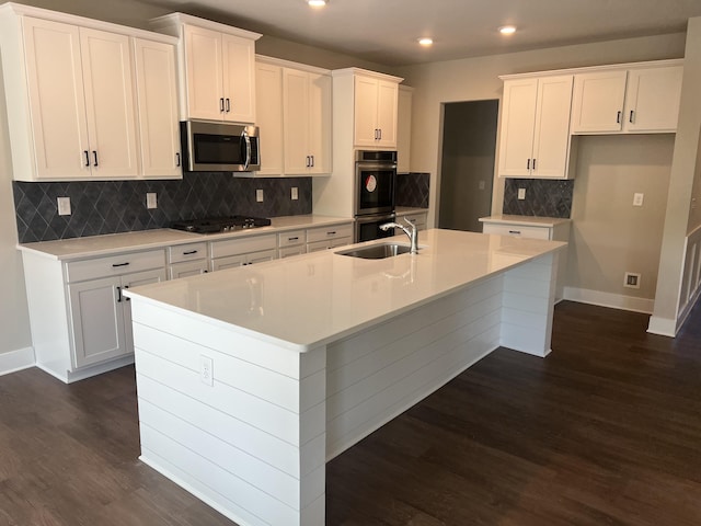 kitchen featuring white cabinetry, sink, dark wood-type flooring, stainless steel appliances, and a kitchen island with sink