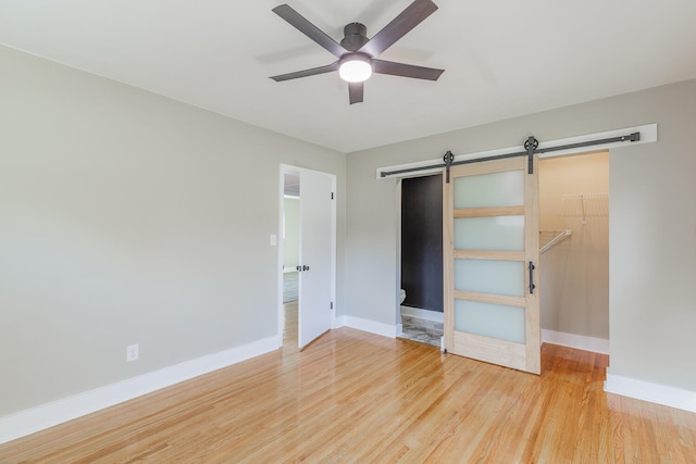 unfurnished bedroom featuring ceiling fan, a spacious closet, a barn door, a closet, and hardwood / wood-style flooring