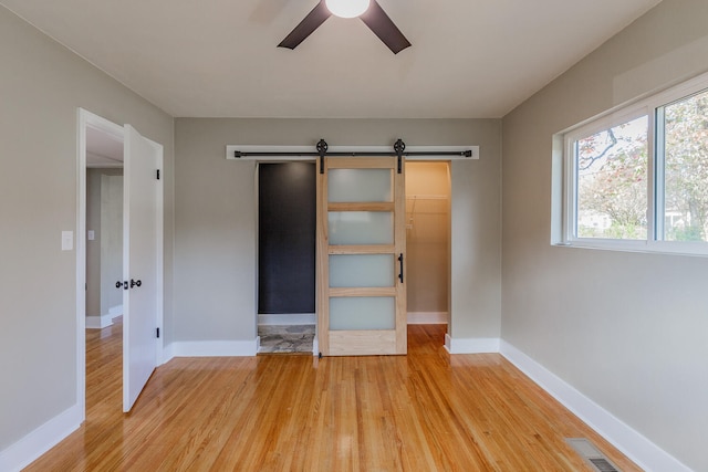 unfurnished bedroom with a walk in closet, ceiling fan, a closet, and wood-type flooring