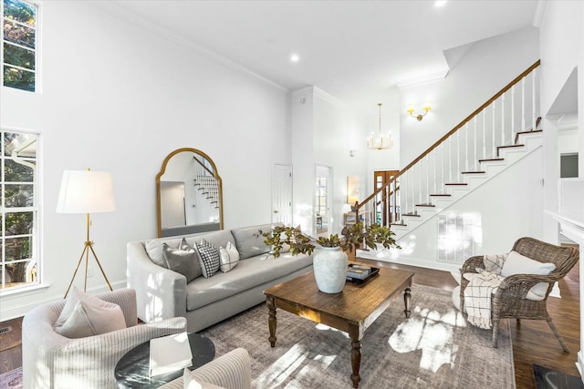 living room with wood-type flooring, a towering ceiling, crown molding, and a notable chandelier