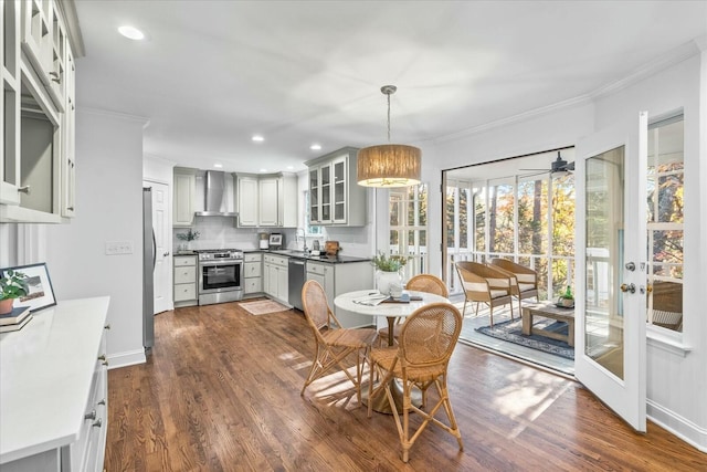 kitchen featuring wall chimney exhaust hood, dark hardwood / wood-style floors, ornamental molding, appliances with stainless steel finishes, and decorative light fixtures